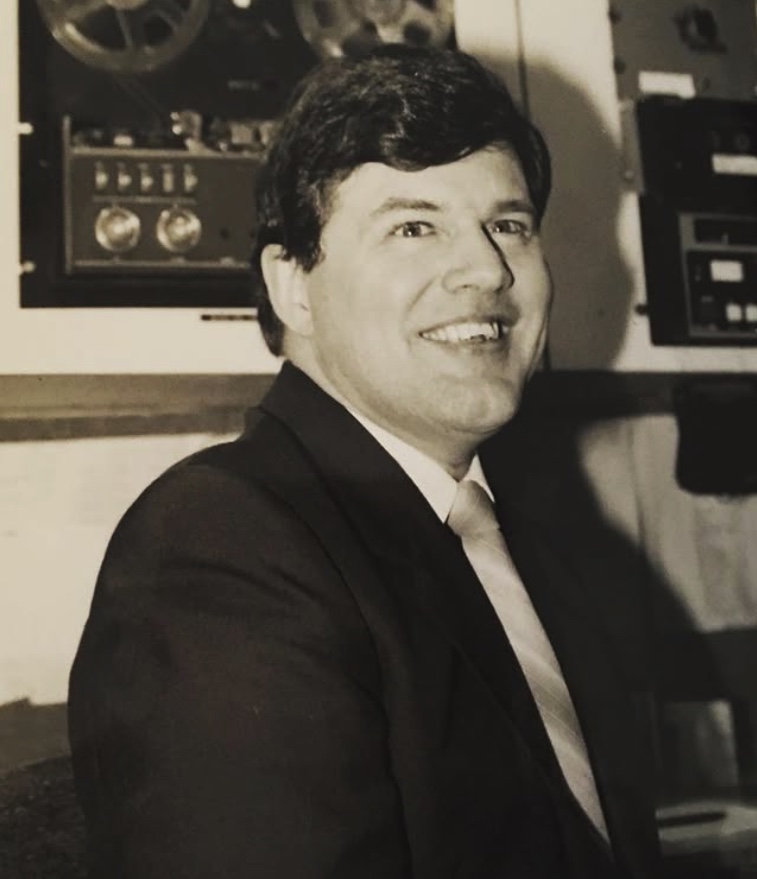 Young Vic Dubois in suit and tie, on the air in front of reel-to-reel tape decks.